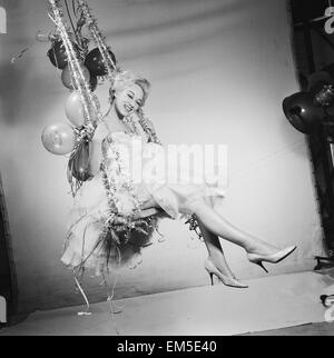 L'actrice Carole Leslie posant dans le studio vêtue d'une robe blanche, assise sur une balançoire avec des décorations de Noël. 24 décembre 1958. Banque D'Images