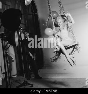 L'actrice Carole Leslie posant dans le studio vêtue d'une robe blanche, assise sur une balançoire avec des décorations de Noël. 24 décembre 1958. Banque D'Images