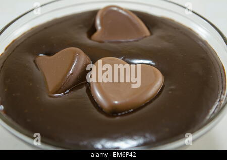 Coeurs en chocolat nageant dans une plaque de verre profonde remplie de chocolat fondu Banque D'Images