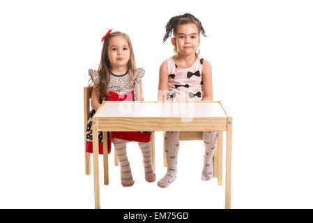 Deux filles assis sur des chaises à la table et faire wry bouche ensemble isolé sur fond blanc Banque D'Images