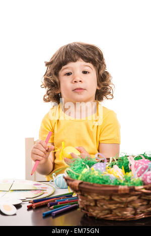 Petit garçon assis sur une chaise et la peinture des oeufs de Pâques isolé sur fond blanc Banque D'Images