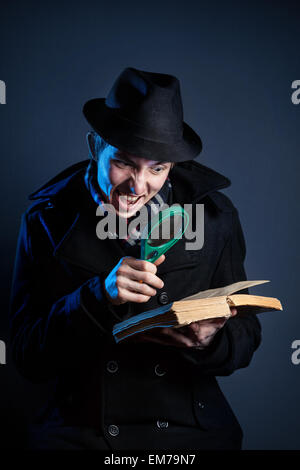 L'homme émotionnel en chapeau noir avec verre loupe lire l'ancien livre à fond sombre Banque D'Images