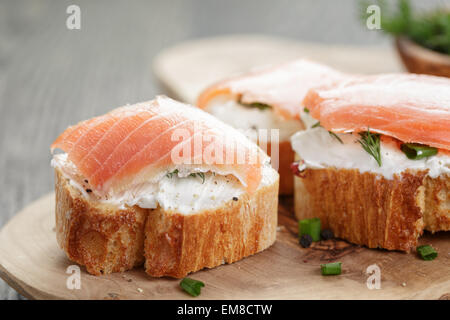 Tranches de baguette avec du saumon fumé et crème de fromage sur la table en bois Banque D'Images