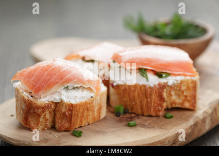 Tranches de baguette avec du saumon fumé et crème de fromage sur la table en bois Banque D'Images