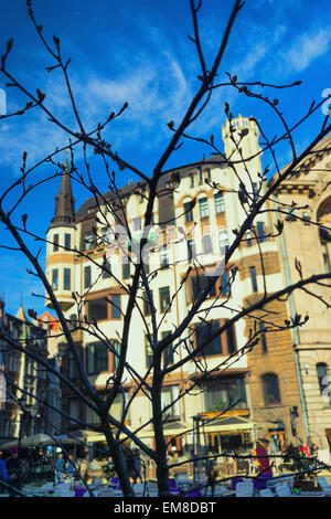 Des bâtiments anciens et des cafés en plein air à travers le web les branches d'arbres sans feuilles sur un jour de printemps à Riga Banque D'Images