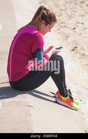 Jeune femme assise à l'aide de téléphone au coureur de la plage de Bournemouth en Avril Banque D'Images