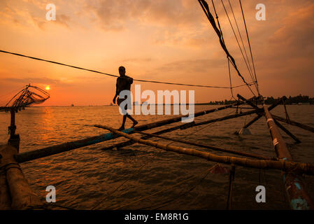 Un pêcheur en silhouette au coucher du soleil, debout sur un filets de pêche chinois à fort Kochi, Kerala Inde Banque D'Images