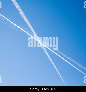 Jet de traînées traînées en X à travers un ciel bleu. Banque D'Images