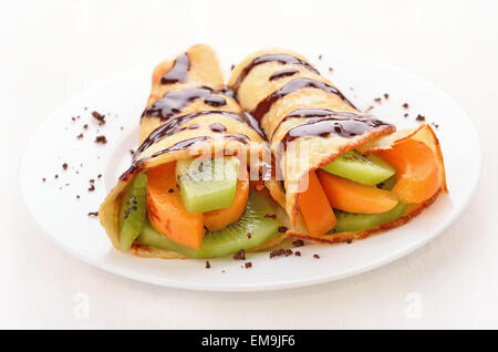 Crêpes avec fruits sur plaque blanche sur table en bois Banque D'Images