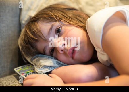 Petite fille avec télécommande tv regarder la télé sur le canapé s'étendait Banque D'Images