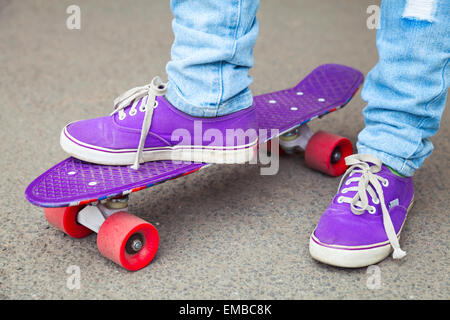 Les jeunes en jeans et gumshoes skateboarder béquilles. Close-up fragment de skateboard et les pieds Banque D'Images