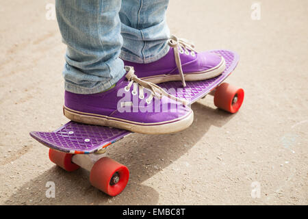 Jeune skateur professionnel en jeans et gumshoes debout sur son skate. Close-up fragment de skateboard et les pieds Banque D'Images