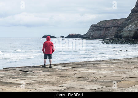 Homme non identifiables portant cagoule rouge sur la jetée en béton, à Whitby, North Yorkshire, Angleterre. Banque D'Images