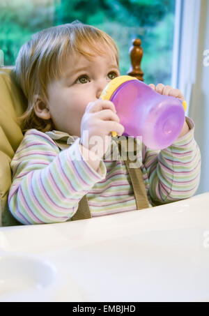 Young Girl (15 mois) d'alcool et de son gobelet, assis sur une chaise, regardant loin à la lumière des frais généraux Banque D'Images