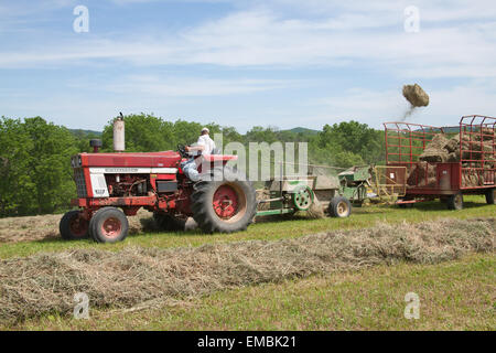 International Harvester Farmall homme sur le tracteur, la mise en balles de foin dans un champ avec un vol de balle en l'air, près de Galena, Illinois, USA Banque D'Images