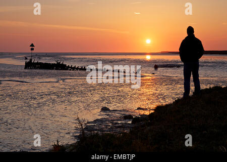 Ruisseau de Faversham, Kent, UK. 20 avril 2015 : Météo France. Un homme regarde la lueur jaune- rouge de l'aube sur une épave dans Faversham Creek près de l'estuaire de Swale comme la marée se retire. Météo ensoleillée va dominer dans le sud-est pour les prochains jours, mais toujours avec une brise fraîche NE Banque D'Images