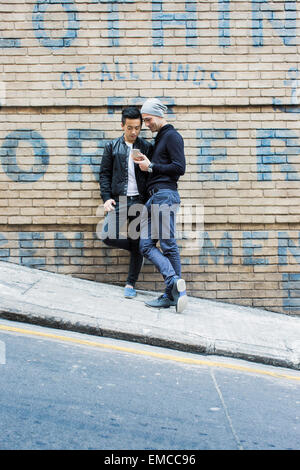 La Chine, Hong Kong, couple gay au mur de la maison à la recherche on cell phone Banque D'Images