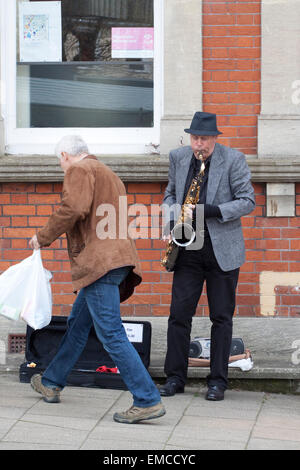 Un musicien ambulant de rue jouant un saxophone ténor comme un passant met l'argent dans son cas Banque D'Images