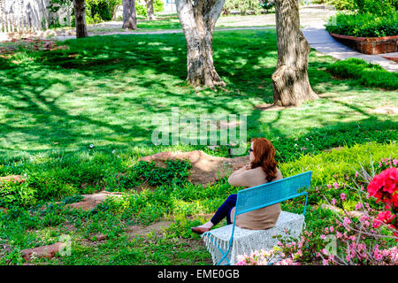 Un blanc, red-haired woman est assis sur un banc et bénéficie d'un printemps de l'aéroport Will Rogers park à Oklahoma City, Oklahoma, USA. Banque D'Images