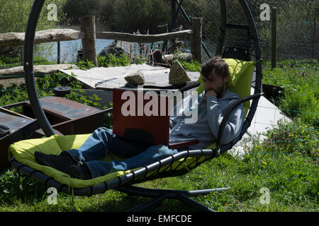 Jeune homme, est la détente à l'extérieur dans le jardin. Faire la révision et les jeux, jouer à un jeu vidéo à l'extérieur. Banque D'Images