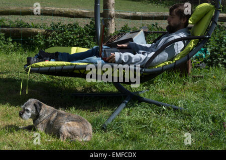 Jeune homme, est la détente à l'extérieur dans le jardin. Faire la révision et les jeux, jouer à un jeu vidéo à l'extérieur, sur un ordinateur portable avec une frontière pose chien rasé Banque D'Images