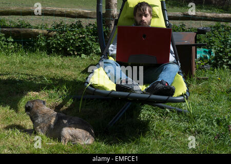 Jeune homme, est la détente à l'extérieur dans le jardin. Faire la révision et les jeux, jouer à un jeu vidéo à l'extérieur sur un ordinateur portable chien border Banque D'Images