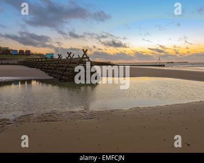 Un magnifique lever de soleil sur la plage à marée basse à partir de la jetée à la jetée dans l'arrière-plan. Banque D'Images