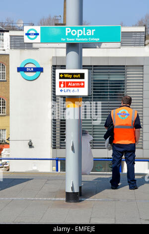 Docklands Light Railway vue arrière employé debout sur la plate-forme de la station Poplar portant une veste haute visibilité avec dépôt DLR et logo au-delà de Londres Royaume-Uni Banque D'Images