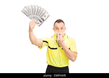 Arbitre de football furieux qui souffle dans un sifflet, tenant une pile de l'argent et regardant la caméra isolé sur fond blanc Banque D'Images