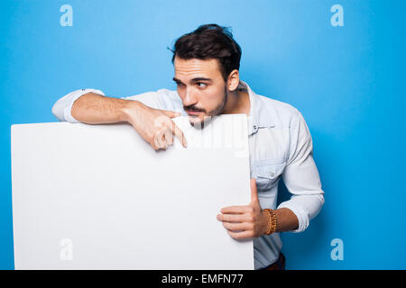 Bel homme avec barbe, à la masculin, avec panneau vierge en face sur fond bleu Banque D'Images