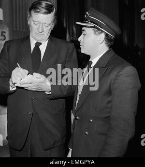 L'acteur américain John Wayne laissant les Ambassadeurs Club à Hamilton, London signe un autographe pour portier Tas d'aulnes. 17 janvier 1974. Banque D'Images