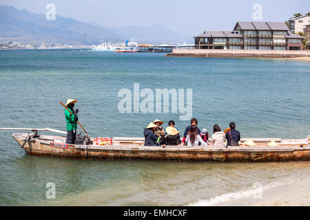 Petit bateau de croisière en mer rouge à travers le torii sacré, les passagers sont à bord de la plage. L'île de Miyajima Banque D'Images