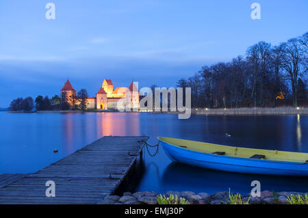 Château de l'île sur le lac Galve allumé au crépuscule en automne avec bateau et quai de premier plan. Trakai, Lituanie Banque D'Images