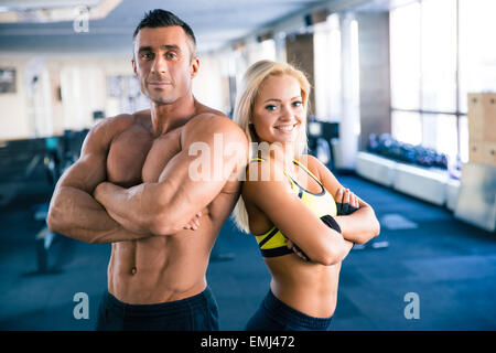 Bel homme musclé et beau sporty woman with arms folded debout dans une salle de sport. Looking at camera Banque D'Images