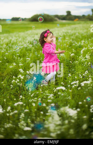 Belle jeune fille insouciante jouant à l'extérieur dans le champ avec une haute herbe verte. petit enfant courir loin de bulles et de rire Banque D'Images
