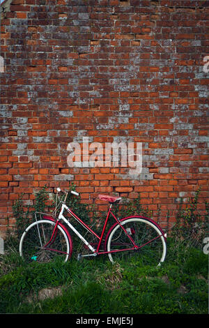 Vélo rouge appuyé contre mur de brique rouge Banque D'Images