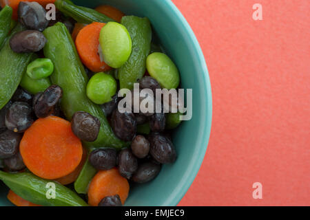 Fermer la vue de carottes au beurre, les haricots noirs, haricots et pois mange-tout dans un bol sur un fond orange. Banque D'Images