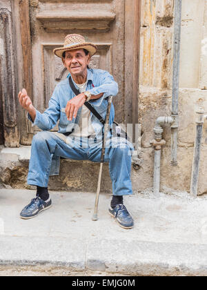 Un mâle cubain Senior citizen des gestes avec sa main droite qu'il s'appuie sur sa canne et se repose sur une mesure concrète de sa maison. Banque D'Images