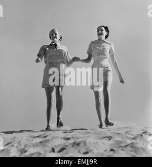 Deux femmes à la mode en short se tenant la main en marchant sur la plage, vers 1952 Banque D'Images