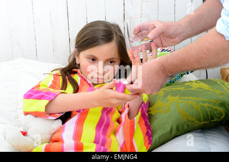 Une petite fille dans le lit en tenant comprimé avec de l'eau Banque D'Images