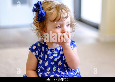 Une petite fille de 14 mois mange un biscuit, assis sur le plancher. Banque D'Images