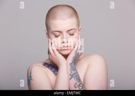 Une jeune femme avec la tête rasée et le tatouage sur son épaule, bras et mains Banque D'Images