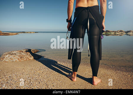 Vue arrière de l'homme debout sur le lac wearing wetsuit. Cropped shot de triathlète se préparer pour une course. Banque D'Images