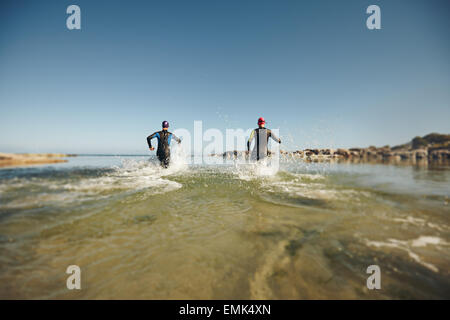 Les participants en marche dans l'eau pour le démarrage d'un triathlon. Deux triathlètes de se précipiter dans l'eau pour nager partie de course. Banque D'Images