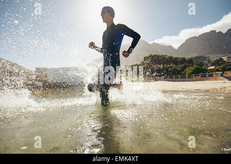 Triathlète masculin courir dans l'eau. La formation pour la compétition de triathlon dans le lac. Banque D'Images