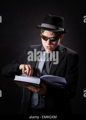 Sérieusement teenage boy dressed in suit la lecture de livre, isolated on black Banque D'Images