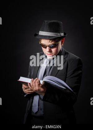 Sérieusement teenage boy dressed in suit la lecture de livre, isolated on black Banque D'Images