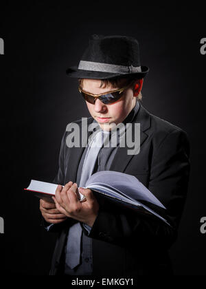 Sérieusement teenage boy dressed in suit la lecture de livre, isolated on black Banque D'Images