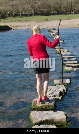 Stepping Stones smartly dressed woman crossing river à l'aide d'une branche d'arbre pour l'équilibre. Balade sur la rivière dans le sud de Ogmore W Banque D'Images