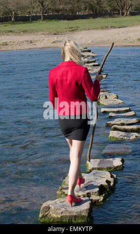 Stepping Stones smartly dressed woman crossing river à l'aide d'une branche d'arbre pour l'équilibre. Balade sur la rivière dans le sud de Ogmore W Banque D'Images